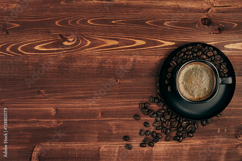 Hot coffee in black cup with crema and beans with copy space on brown old wooden board background, top view. Rustic style.