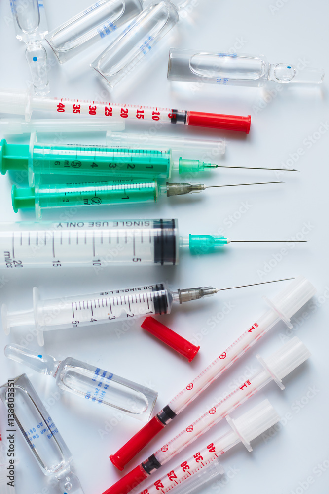 Plastic syringes with needles of different sizes and glass ampoules with medicine isolated on white background Plastic syringes with needles of different sizes and glass ampoules with medicine isolated on white background