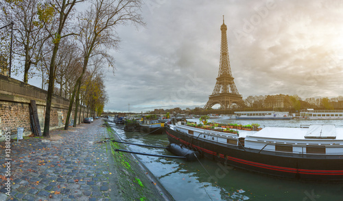 Beautiful panoramic view of the Eiffel Tower and Jena bridge from the river Seine embankment. Dramatic cloudscape. Traditional citycape in backlit morning sunbeam. Paris, France.