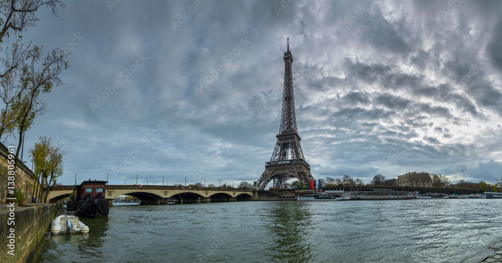 Fototapeta premium Panoramic view of the Eiffel Tower and Jena bridge from the river Seine embankment. Dramatic cloudscape. Paris, France.