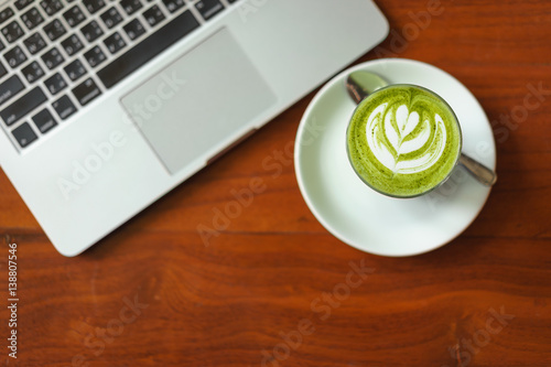 Breakfast with hot matcha green tea latte and laptop in background on wooden table