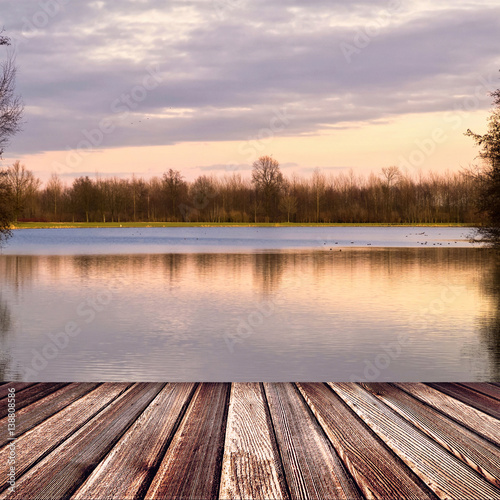 Fototapeta Naklejka Na Ścianę i Meble -  Wooden deck floor on sunset lake with trees and sky