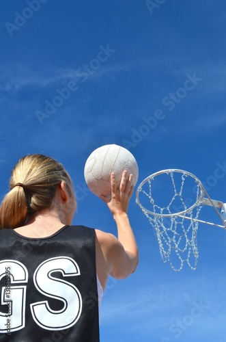 Blond caucasian woman shoots a netball into a netball ring