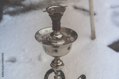 Big hookah for tobacco made of metal, glass and ceramics. Snowing. Snow background. White photo