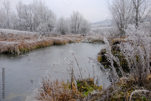 Winter landscape with frosted small lake and noarfrost covered plants and trees