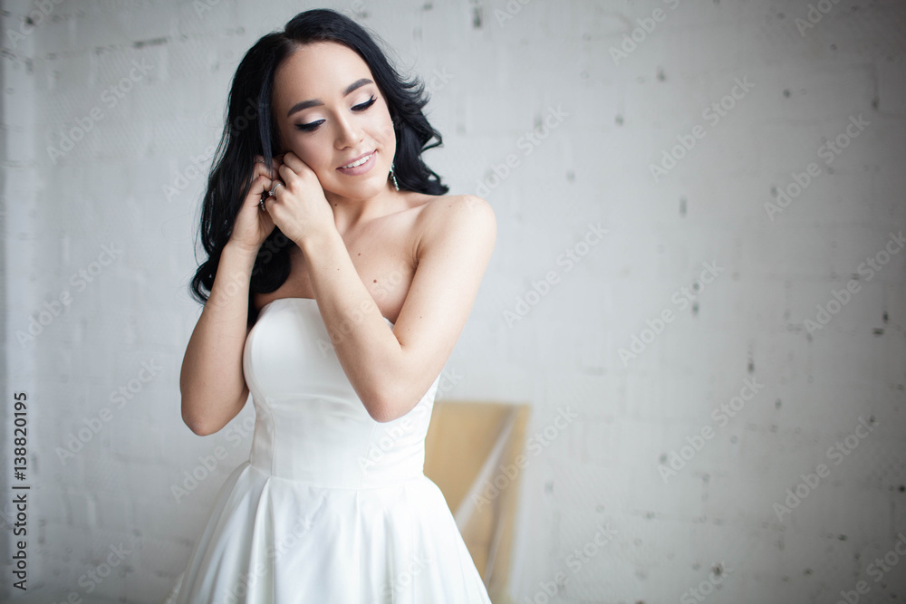Tanned beautiful brunette bride wears earrings. Model with long dark hair. Studio portrait on white background. Tanned beautiful brunette bride wears earrings. Model with long dark hair. Studio portrait on white background.