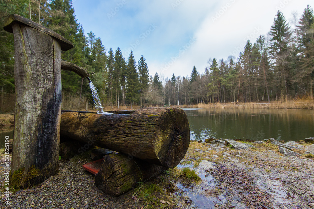 water fountain built of wood in the forest with lake, clouds, blue sky water fountain built of wood in the forest with lake, clouds, blue sky