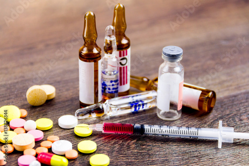 Drugs addiction concept. Drugs injection. Pills, injector, ampules isolated on wooden background photo