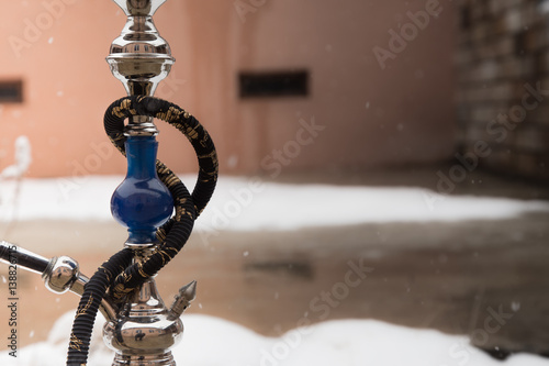 Big hookah for tobacco made of metal, glass and ceramics. Snowing. Snow background. White photo