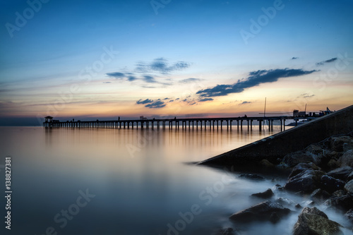 Dark rock dam in blue ocean on twilight sunset and wooden bridge extended into the sea with water reflection., long exposure photography., the concept of lonely, sadness, depressed and broken heart.