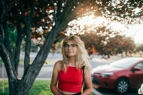 A blonde girl in glasses standing in the park in sunset