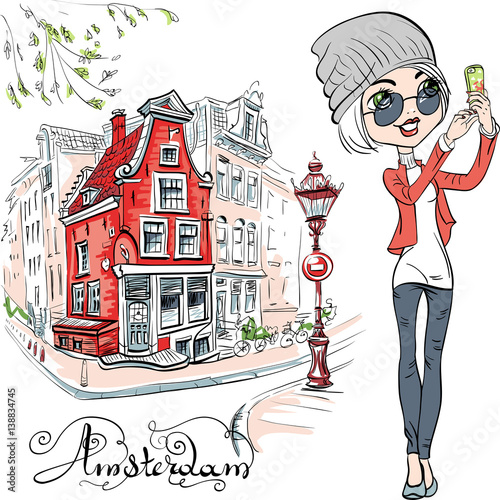 Cute hipster girl makes selfie, street in Amsterdam with traditional Dutch house and streetlight on the background, Holland, Netherlands.