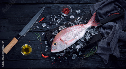 Fresh spanish bream fish (breca) on ice on a black wooden table top view photo