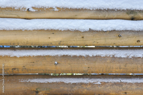 Wooden wall made of round logs. Under the snow