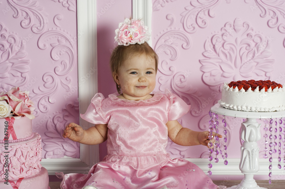 Fototapeta premium Portrait of cute baby girl in pink dress with gourmet cakes. Kid looking in camera
