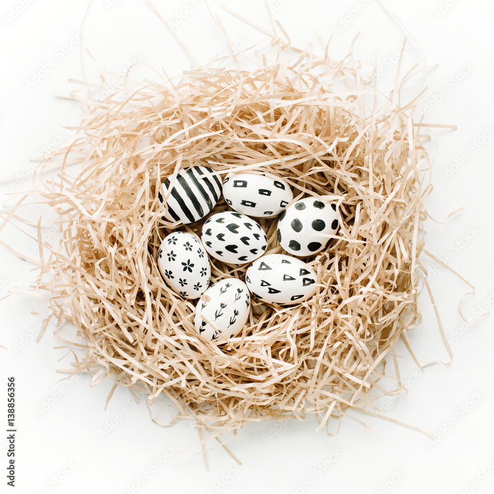Obraz premium Fancy Easter eggs in nest on white background. Flat lay, top view. Traditional spring concept.