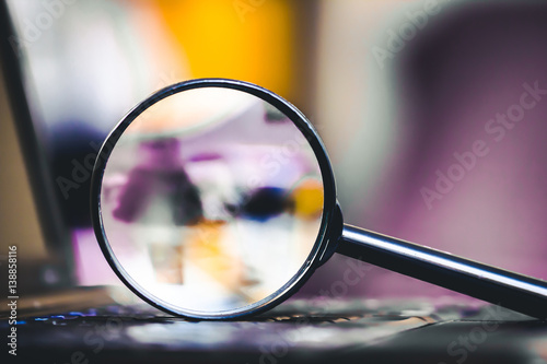 Technology search background. Magnifying glass on computer keyboard with shallow depth of field and blurred colors inside.