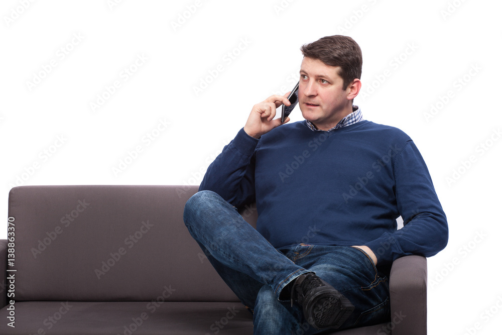 Young man sitting on sofa and talking on phone, isolated on white