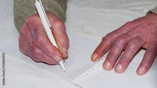 Closeup of the wrinkled hands of an old caucasian man holding pen and paper