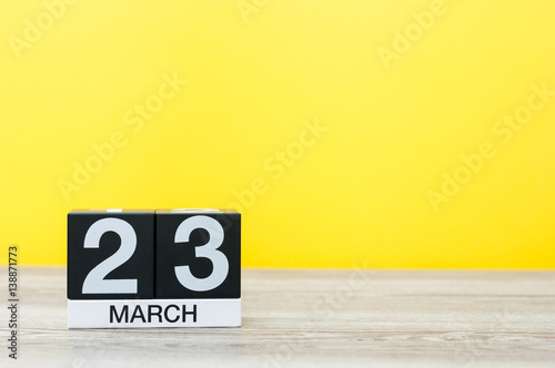 March 23rd. Day 23 of month, calendar on table with yellow background. Spring time, empty space for text