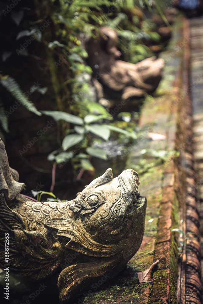 Fish sculptures in ancient overgrown tropical asian garden