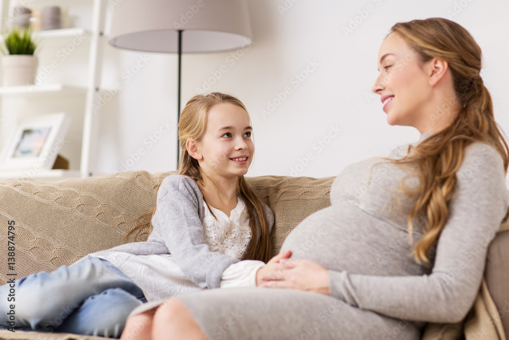happy pregnant woman and girl on sofa at home
