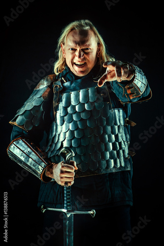 Powerful blond knight with the sword on the dark background