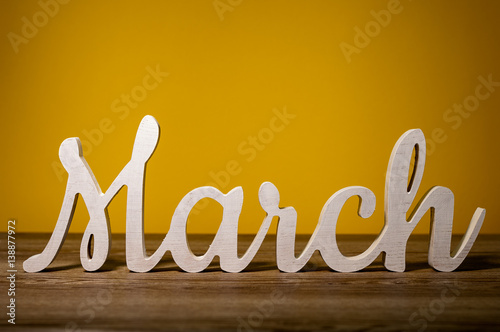 March - first month of spring. Word carved out of wood at orange warm background photo