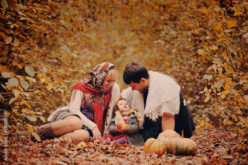 Молодые родители сидят в осеннем лесу со своей маленькой дочерью