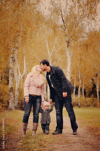 Молодые родители держат на руках маленькую дочь в осеннем парке © oes