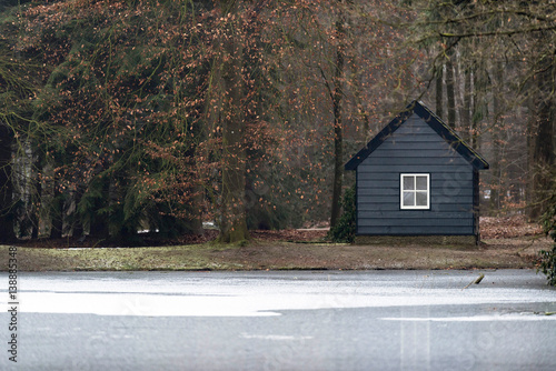 Little wooden cabin at frozen lake in forest.