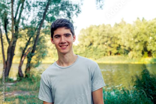A young man with black hair smiling. Portrait of a gay in nature. Sunny sunset behind the man.
