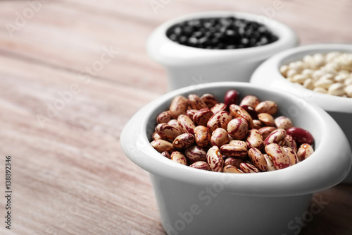 Assortment of haricot beans in bowls on wooden table, closeup