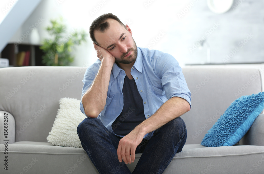 Handsome depressed man sitting on sofa at home Handsome depressed man sitting on sofa at home