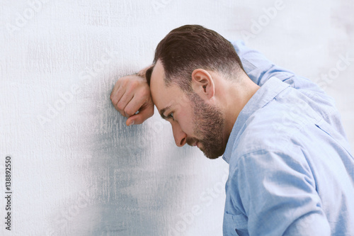 Handsome depressed man standing near wall at home