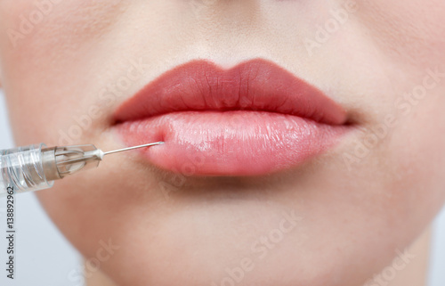 Beautiful young woman receiving filler injection in lips, closeup photo