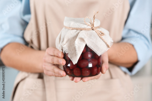 Woman in apron holding jar with jam, closeup