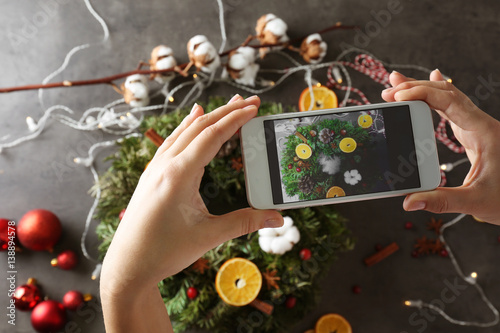 Female hands taking photo of Christmas wreath on table