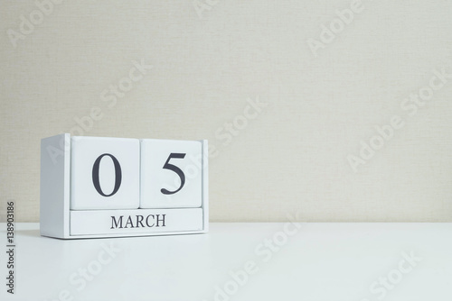 Closeup white wooden calendar with black 5 march word on blurred white wood desk and cream color wallpaper in room textured background with copy space , selective focus at the calendar