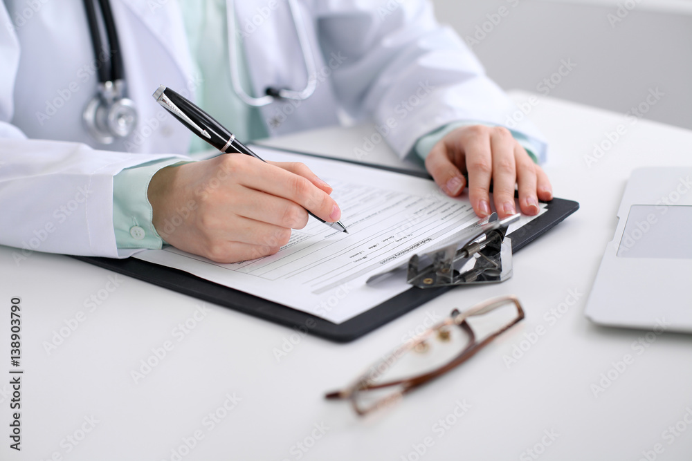 Close-up of a female doctor filling out application form , sitting at the table in the hospital Close-up of a female doctor filling out application form , sitting at the table in the hospital