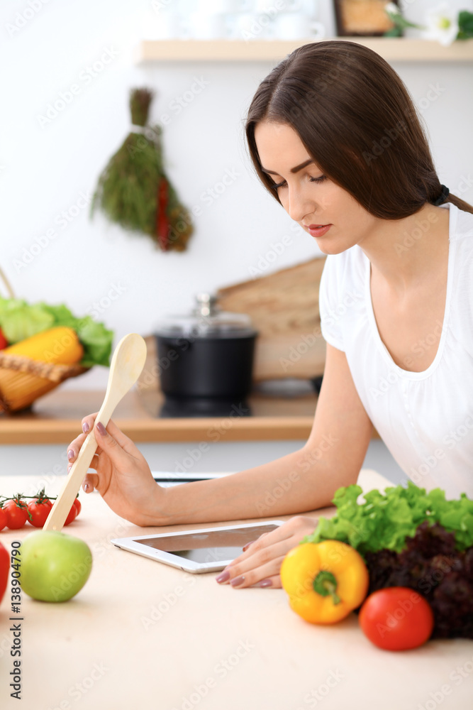Beautiful Hispanic woman is making online shopping by tablet computer and credit card or searching internet for a new recipe. What to cook for a dinner? Beautiful Hispanic woman is making online shopping by tablet computer and credit card or searching internet for a new recipe. What to cook for a dinner?
