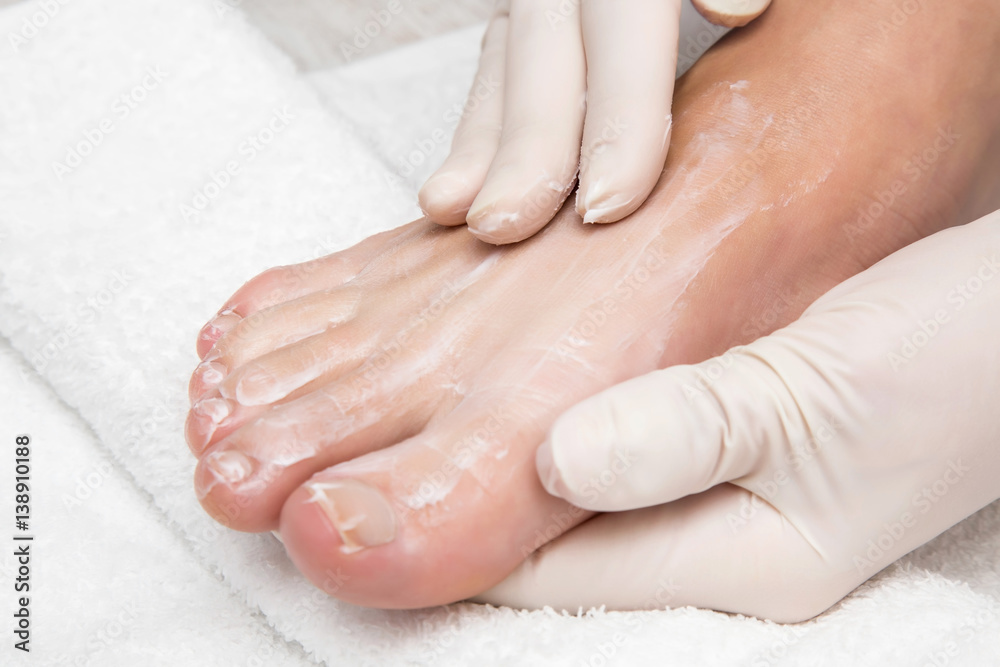 Hands in gloves cares foot nails. Pedicure beauty salon. Foot moisturizing cream.