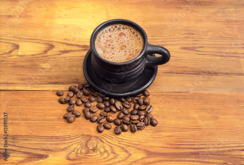 Coffee in black cup and coffee beans on wooden surface