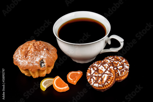 Cake, marmalade, chocolate chip cookies and a cup of coffee on a black background