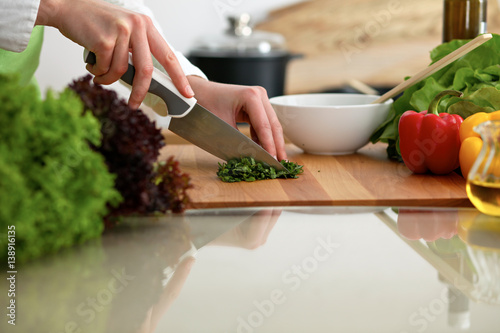 Closeup of human hands cooking vegetables salad in kitchen on the glass table with reflection. Healthy meal and vegetarian concept