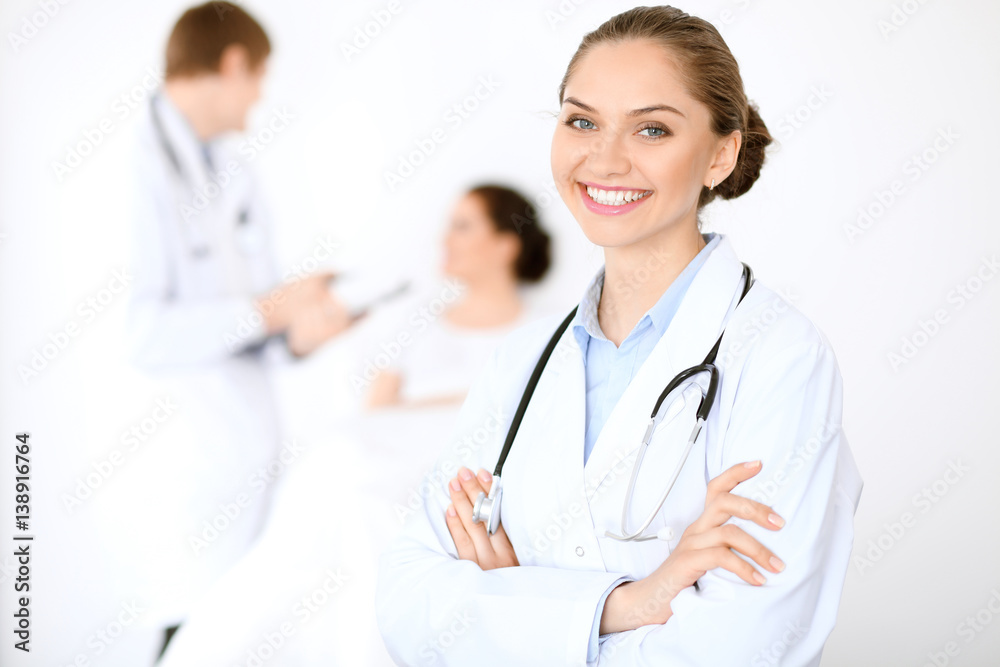 Cheerful smiling female doctor on the background with physician and his patient in the bed. High level and quality of medical service concept. Cheerful smiling female doctor on the background with physician and his patient in the bed. High level and quality of medical service concept.
