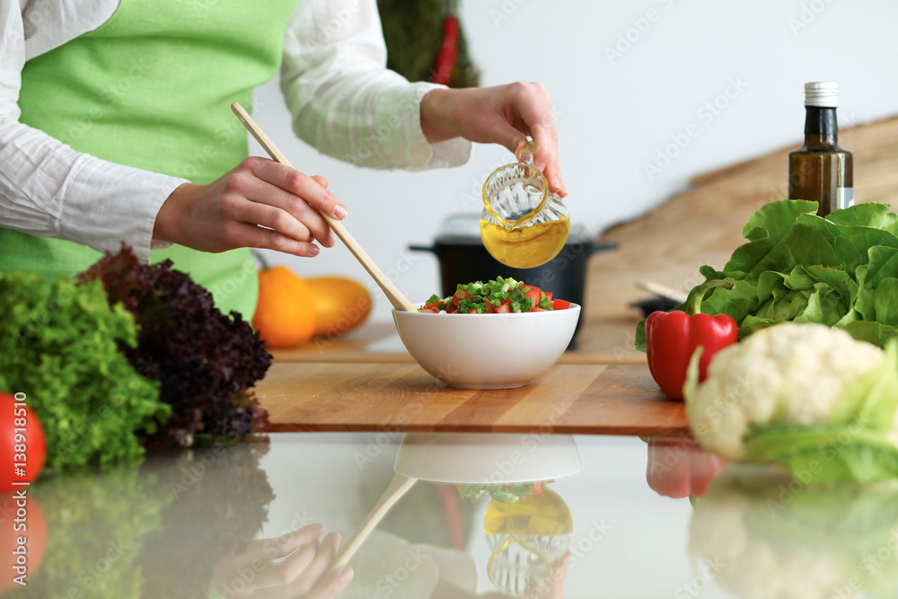 Closeup of human hands cooking vegetables salad in kitchen on the glass table with reflection. Healthy meal and vegetarian concept