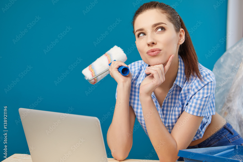 Young woman portrait while painting new apartment ,looking in laptop Young woman portrait while painting new apartment ,looking in laptop