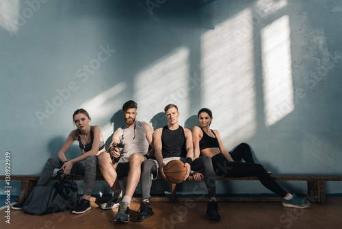 serious sporty men and women sitting on bench in gym