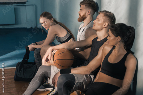 side view of sporty men and women sitting on bench in gym